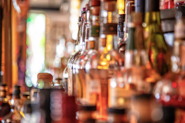A large group of liquor bottles on display on a shelf, all bottles unrecognizable shot with an extremely shallow depth of field for a blurred background and foreground.